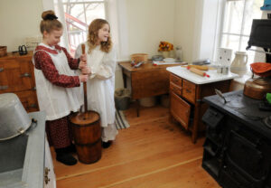 Bown House Children dressed in period clothing making butter in the kitchen of the Bown House